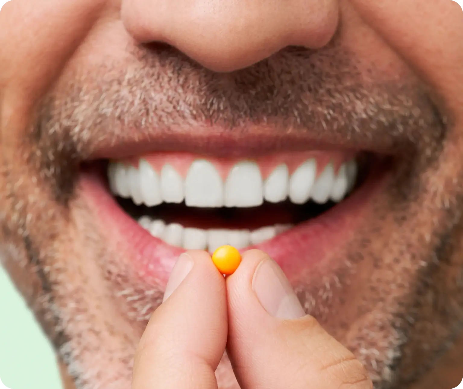 Man smiling while holding a small orange pill near his mouth.