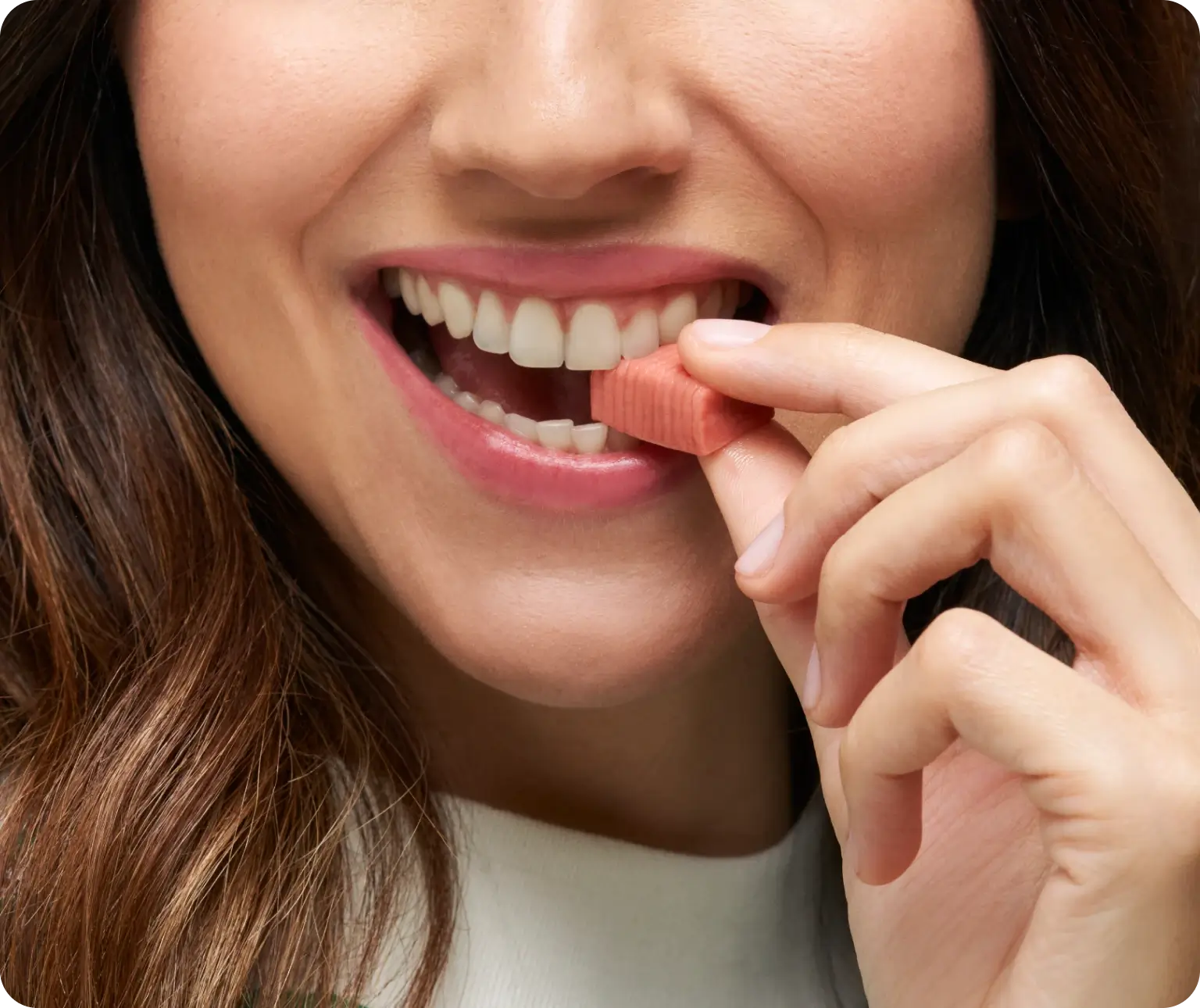 A person smiling while holding a pink chewing gum between their teeth.