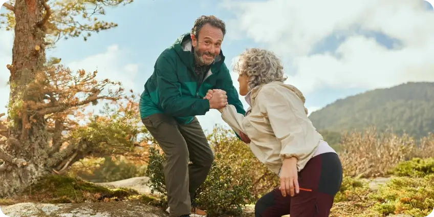 A man helps a woman up a hill while they are hiking outdoors.