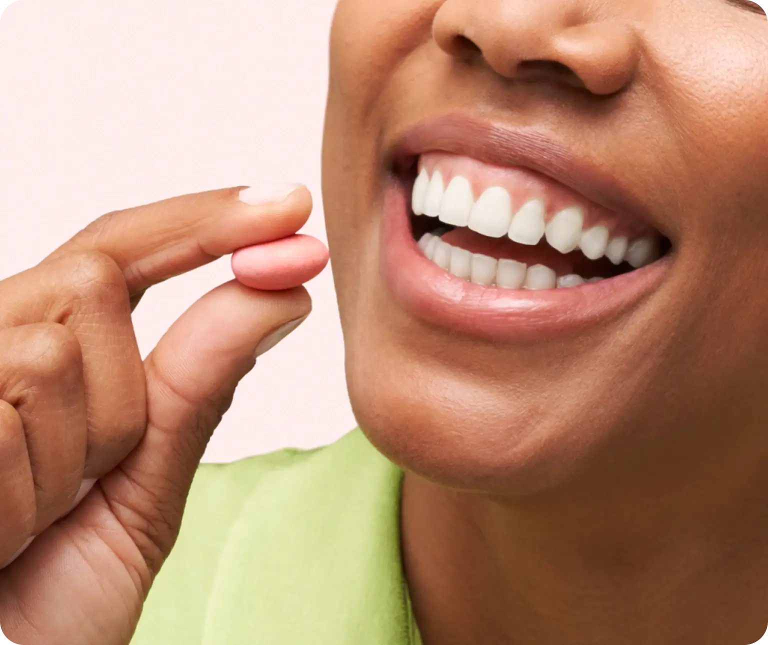 Person smiling while holding a pink pill near their mouth.