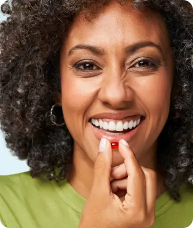 Person smiling, holding a small red capsule near their mouth.