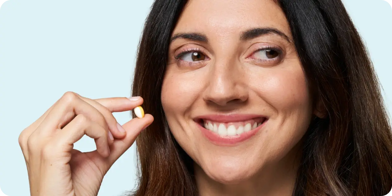 Woman holding a small yellow and white capsule, smiling with a relaxed expression.