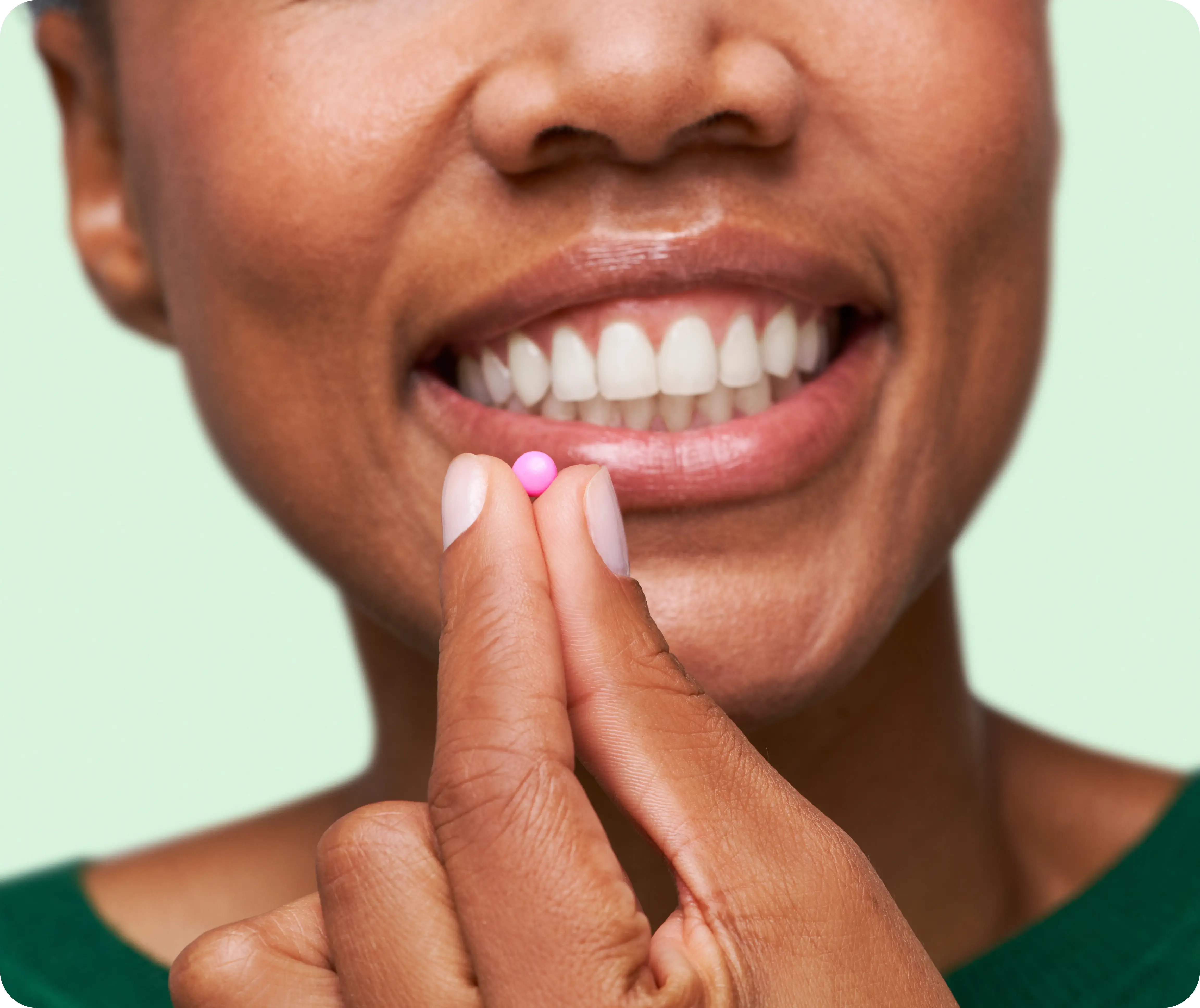 Person holding a small pink pill near their smiling mouth.