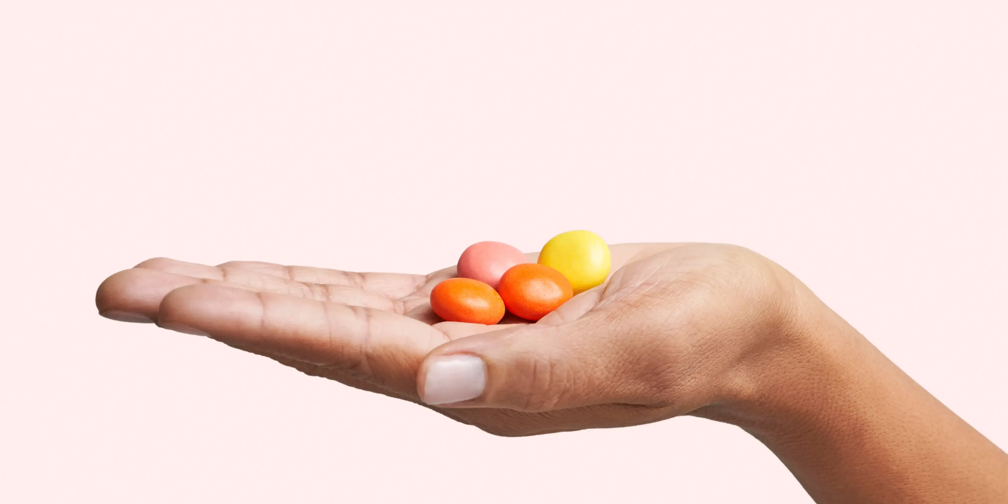 Hand holding colorful small round pills on a light background.