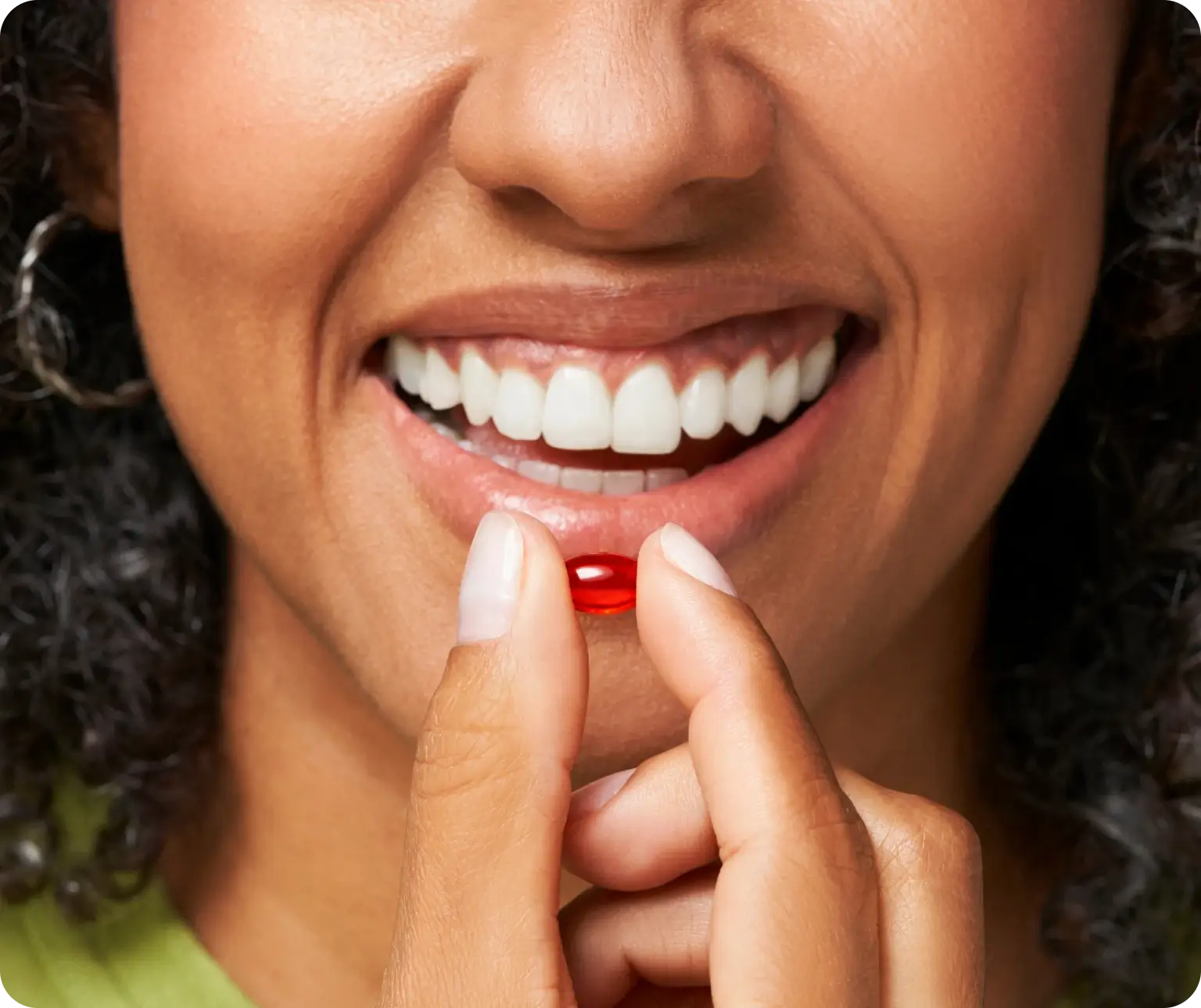 A person smiling while holding a red capsule close to their lips.