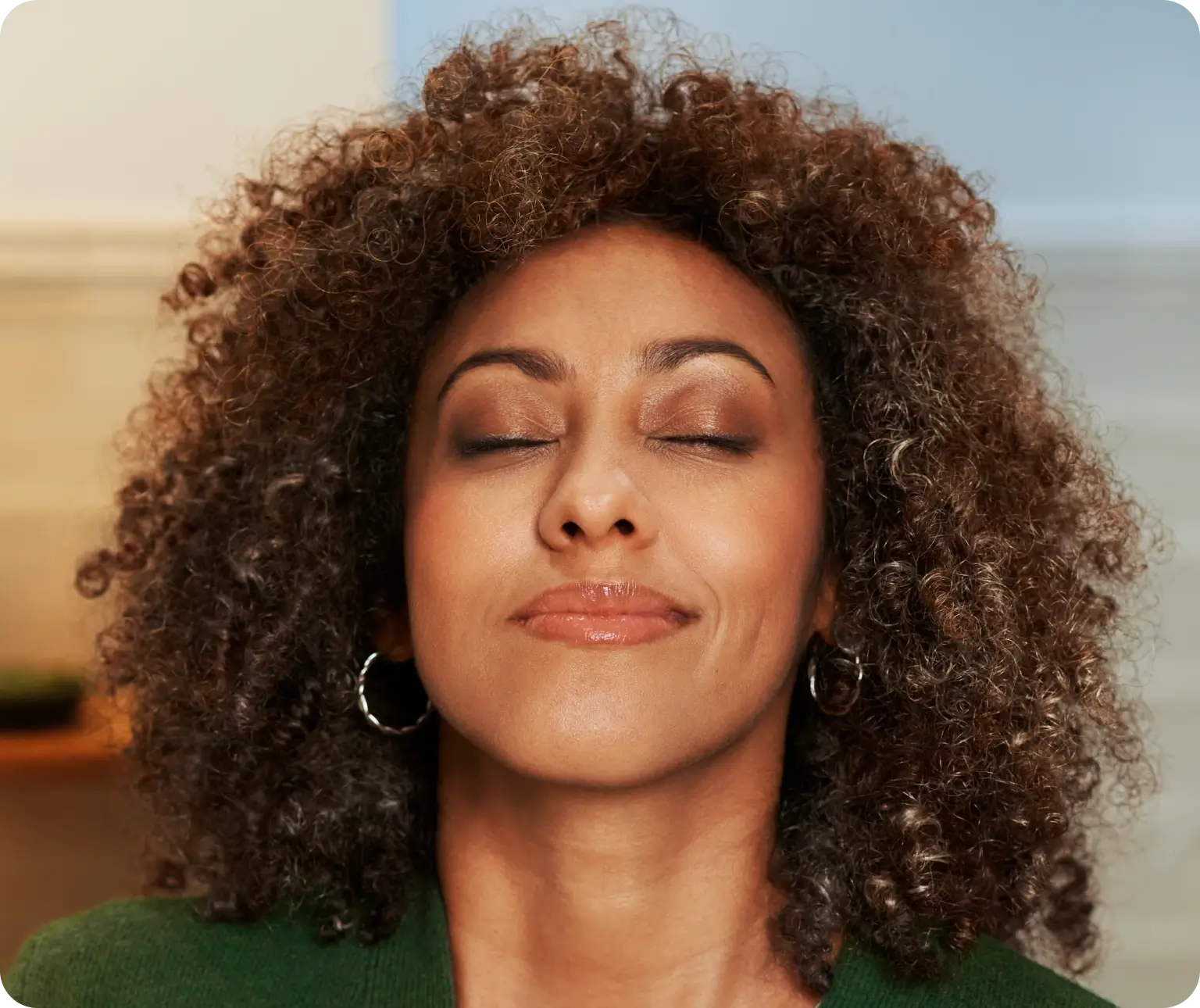 Woman with curly hair smiling with eyes closed, appearing relaxed.