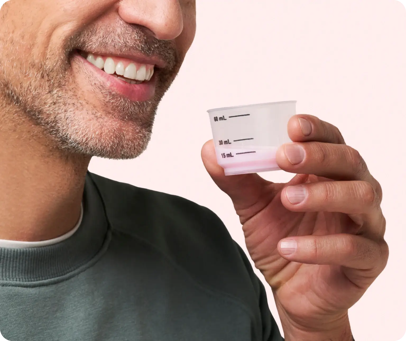 Person holding a 60 mL measuring cup with liquid, smiling slightly.